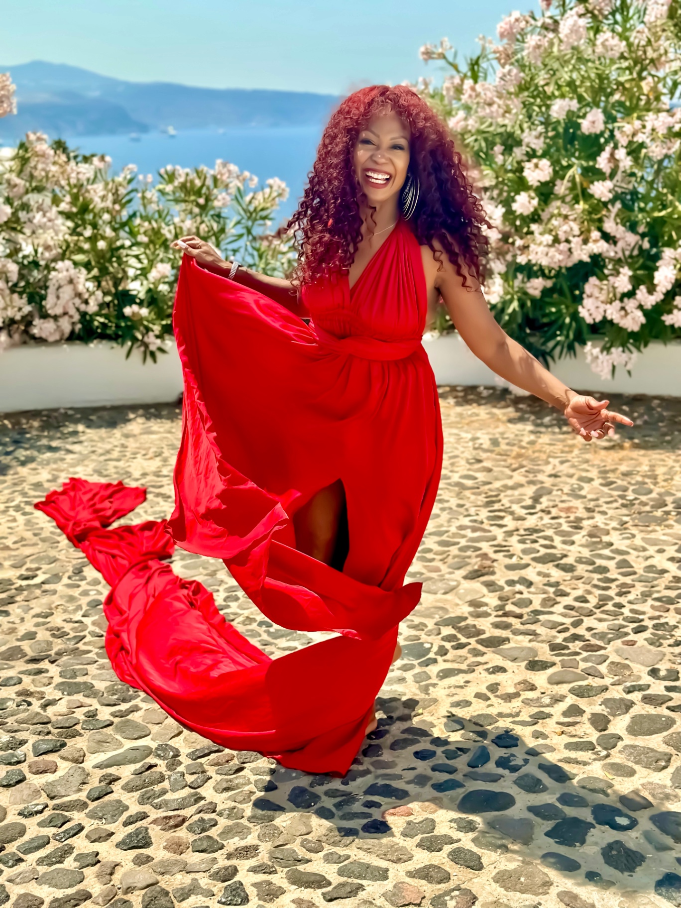 Demishia, travel advisor, in a flowing red dress above the sea in Santorini